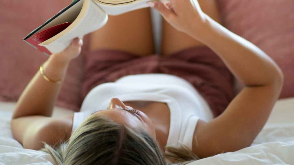 Chica tumbada leyendo un libro.