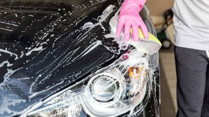 Persona limpiando con agua y jabón el faro del coche.