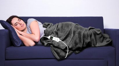 Una mujer descansa caliente con una manta eléctrica en un sofá.