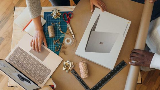 Dos personas envolviendo en papel de regalo un ordenador portátil.