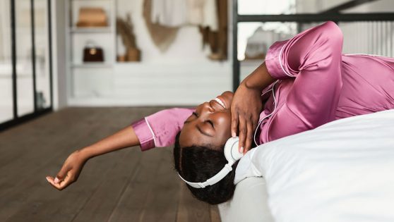 Mujer tumbada en la cama escuchando música con unos cascos.