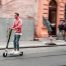 Dos hombres circulando con un patinete eléctrico por la calle.