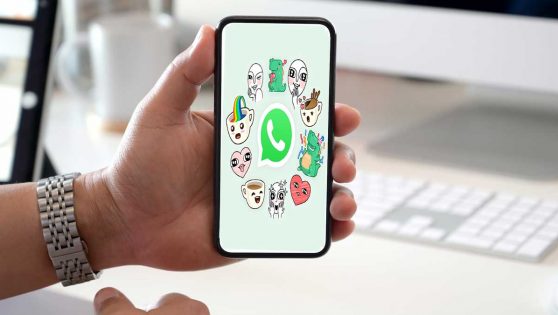 Una persona sujetando un móvil con el logo de WhatsApp y unos stickers en la pantalla.
