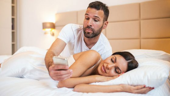 Un hombre espiando el móvil de su pareja mientras duerme y sin su consentimiento.
