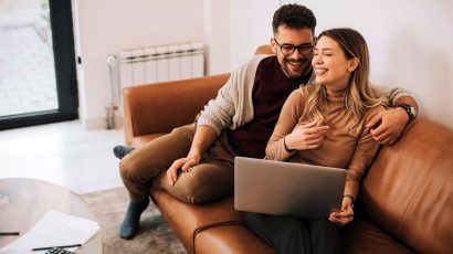 Una pareja en el sofá de su casa consultando el ordenador.