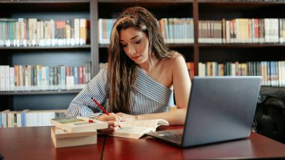 Una chica estudiando en la biblioteca con su ordenador.