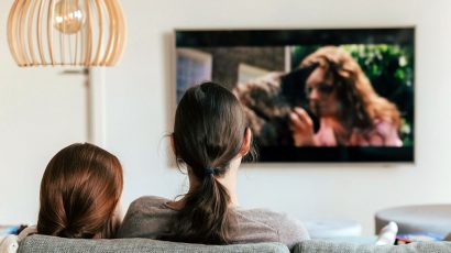 Una madre y una hija sentadas en el sofá viendo una película en la televisión.