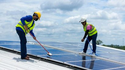 Unos profesionales de limpieza subidos en un tejado limpiando placas solares.