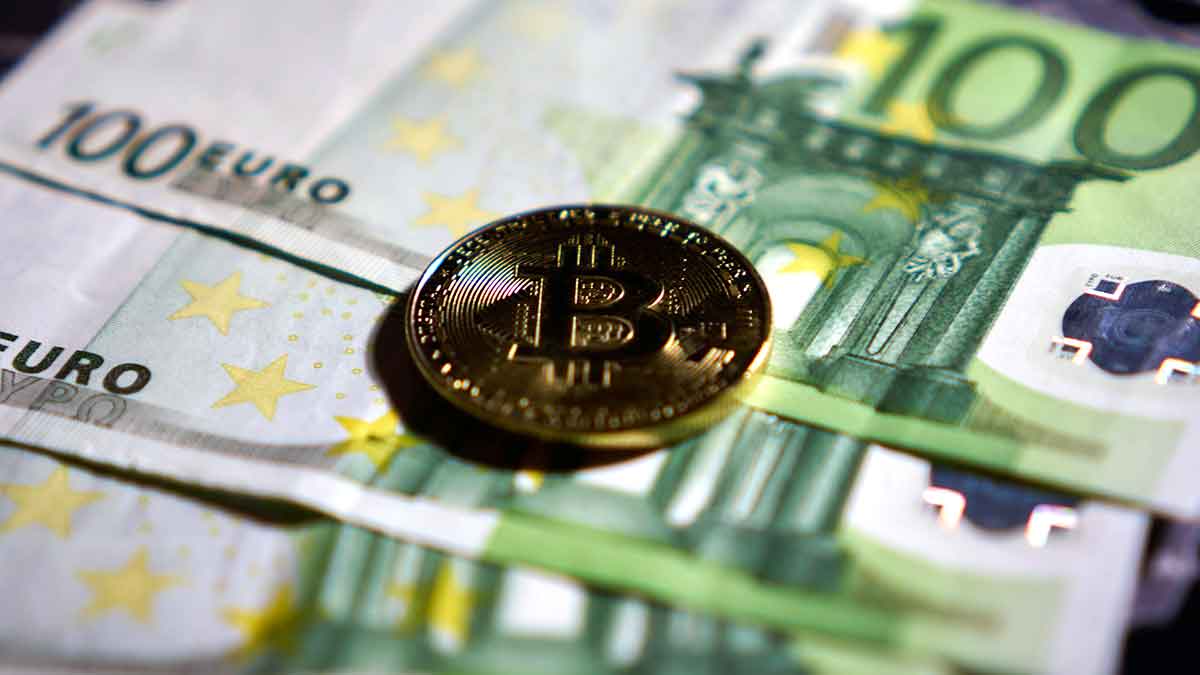 Un Bitcoin en foma de moneda junto a billetes de 100 euros.