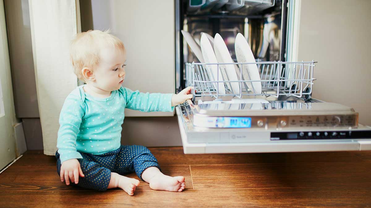 Un bebé junto a un lavavajillas.