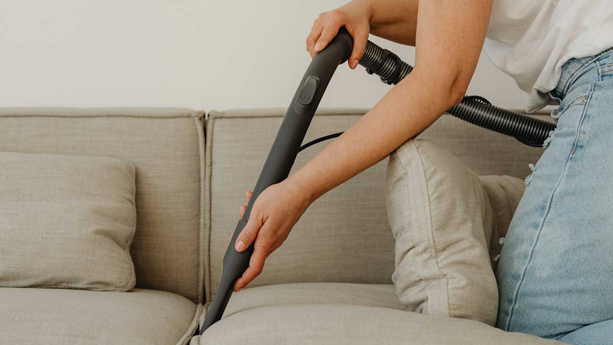 Una mujer pasa la aspiradora por el sofá.